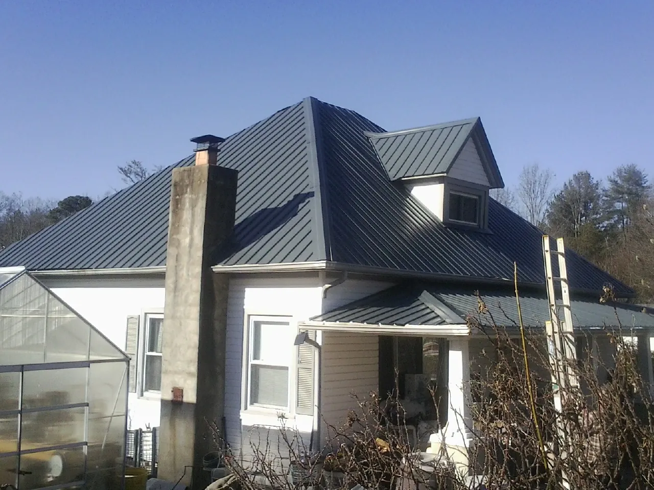 Dark blue standing seam metal roof on a white farmhouse with dormer — Slate & Tile Roof Repair by Roofing Brothers in Cedar Falls