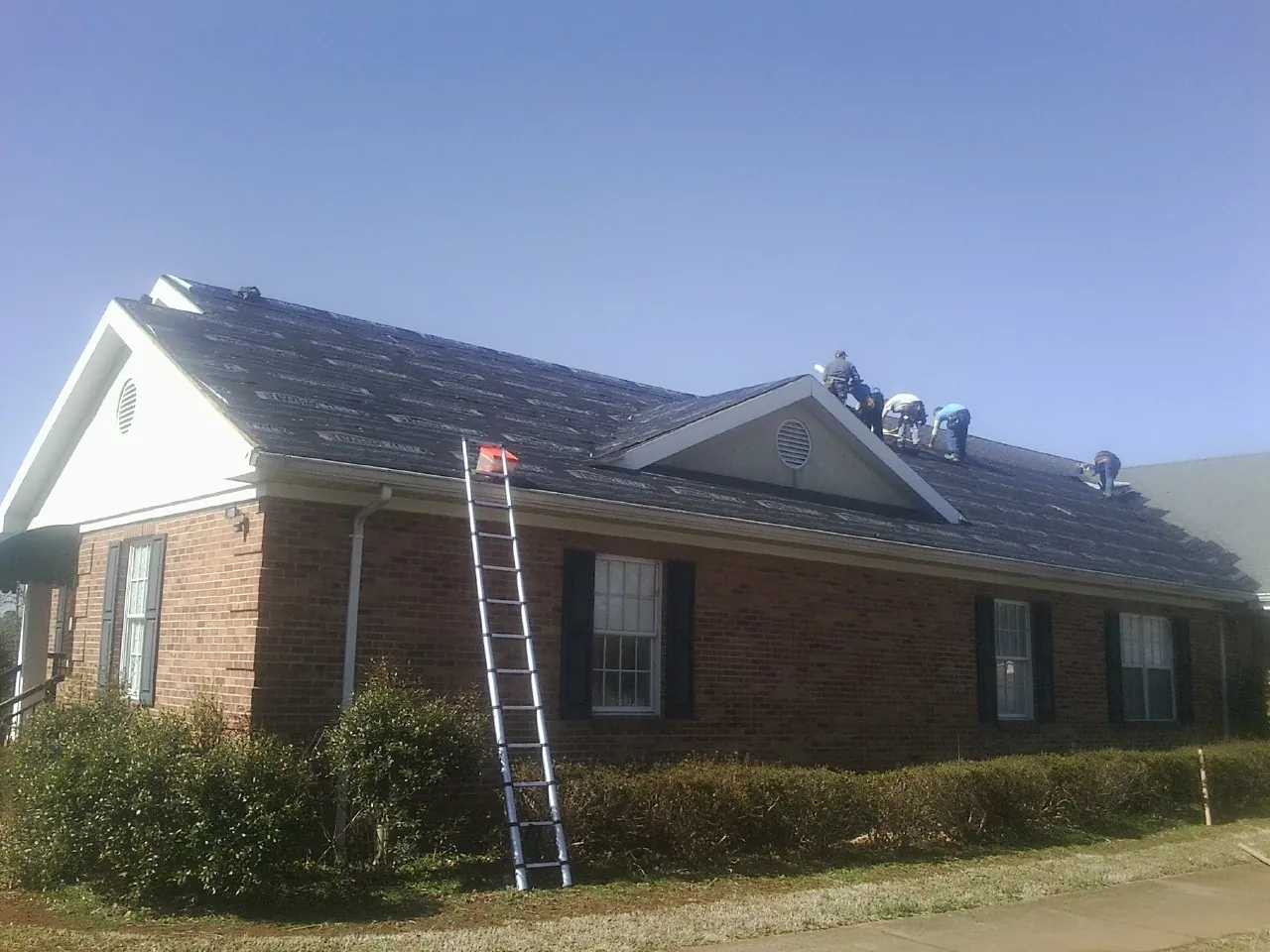 Crew tearing shingles off a brick ranch roof with a ladder set — Emergency Roof Repair work by our crew in Cedar Falls