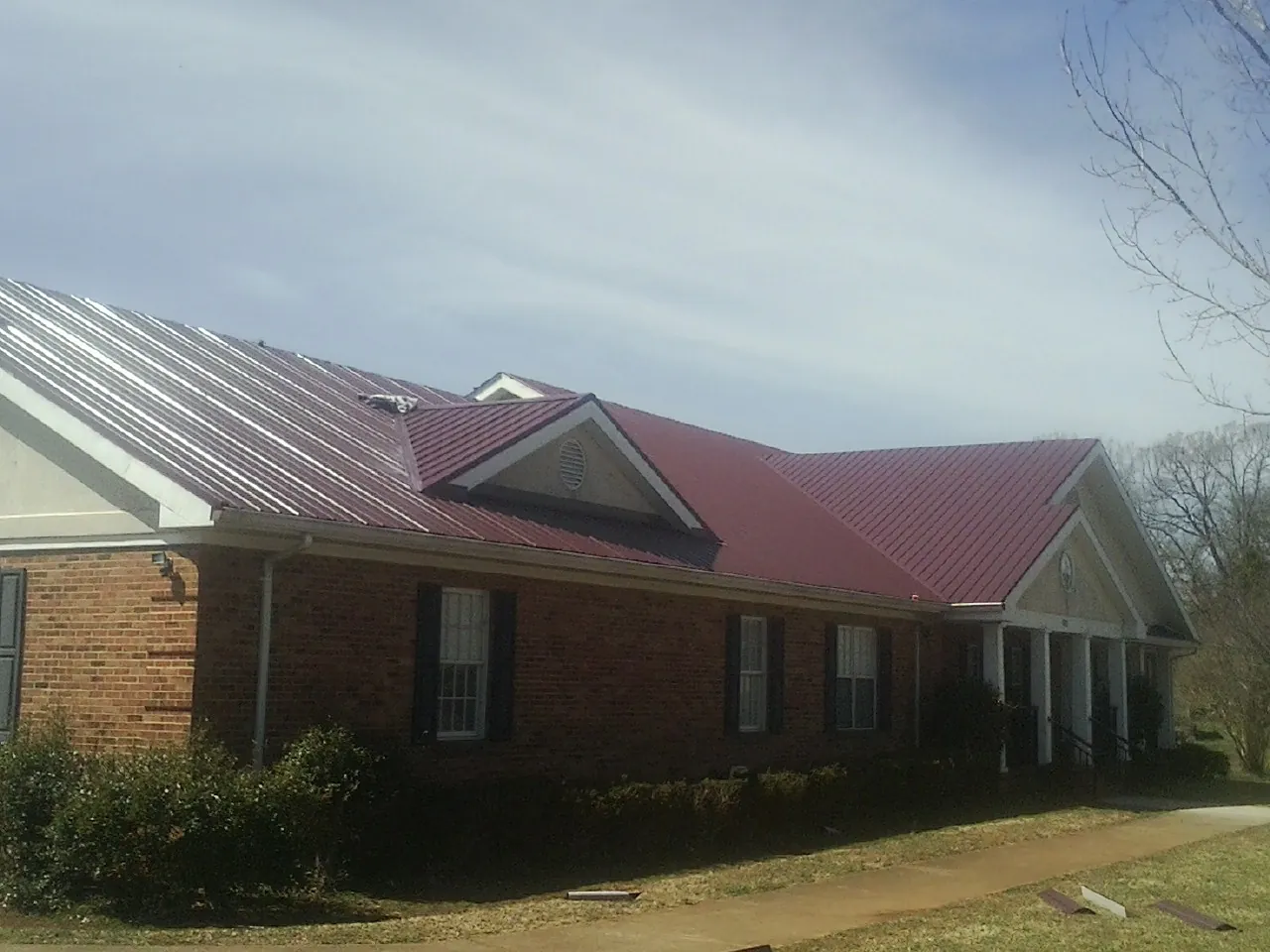 Red metal roof with gabled entries on a long brick building, from a Hail Damage Roof Repair job in Cedar Falls