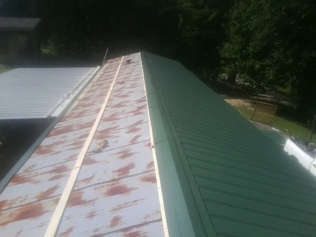 Old rusted panels beside newly installed green metal roofing — Wind Damage Roof Repair by Roofing Brothers in Cedar Falls