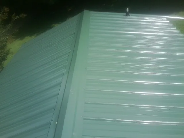 New green metal panels meeting at the ridge of a roof — Flat Roof Repair work by our crew in Cedar Falls