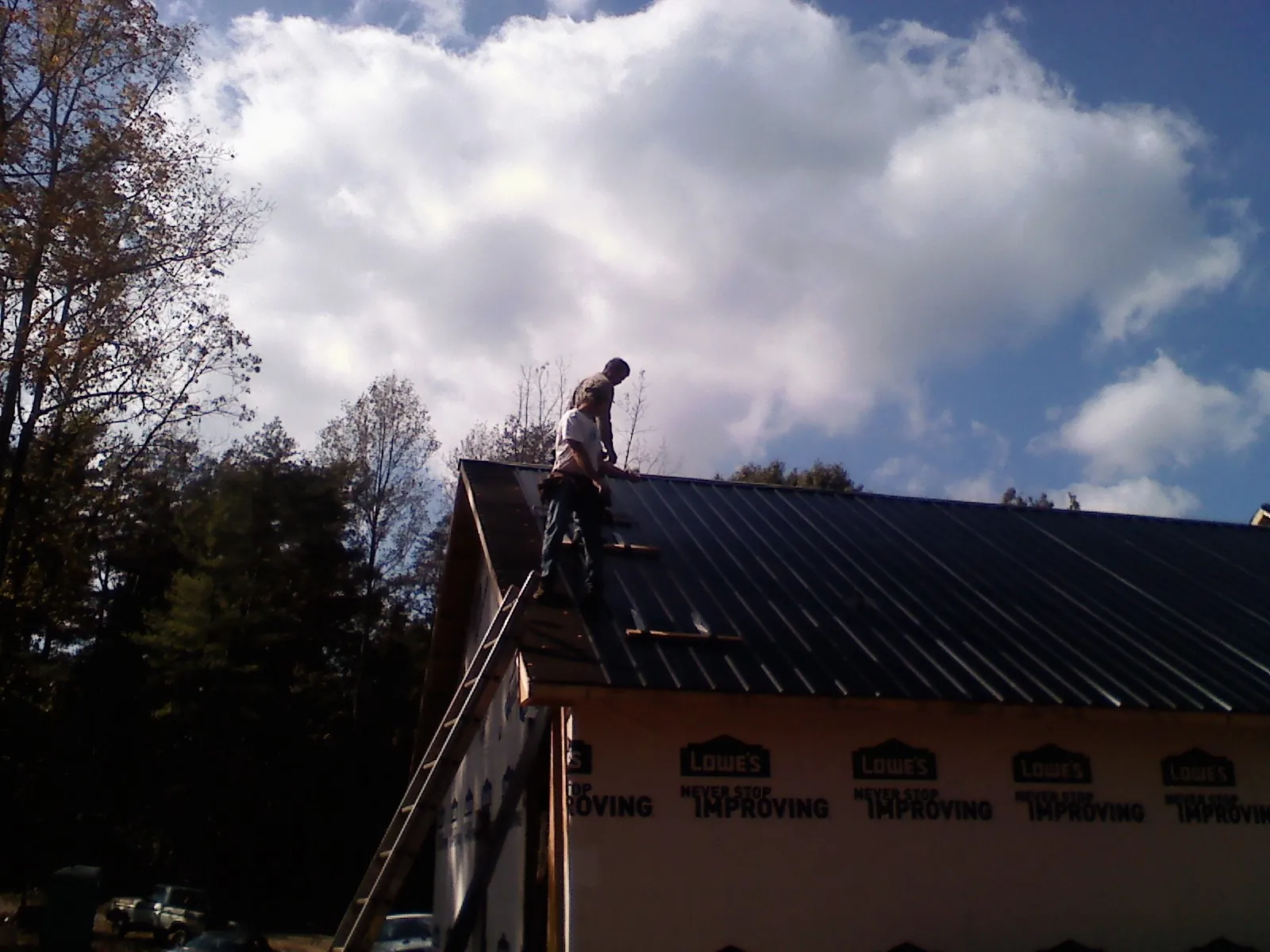 Roofer fastening dark metal panels high against a cloudy sky, from a Roof Inspection job in Cedar Falls