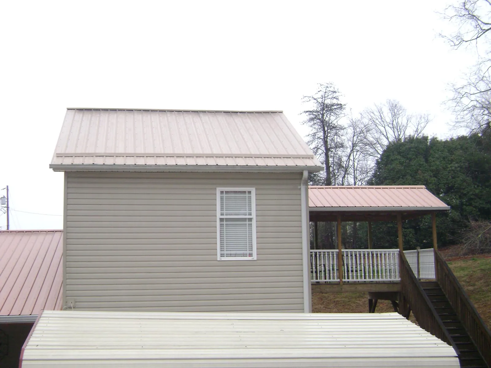 Tan metal roofs on a two story addition and attached porch, from a Roof Replacement job in Cedar Falls