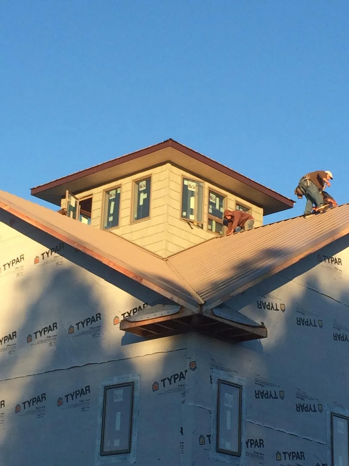 Roofers working around a rooftop cupola on a new metal roof at sunset — Roof Waterproofing in Cedar Falls by Roofing Brothers